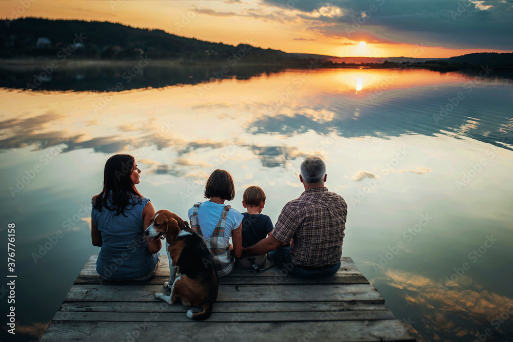 Family sitting together on a dock at sunset